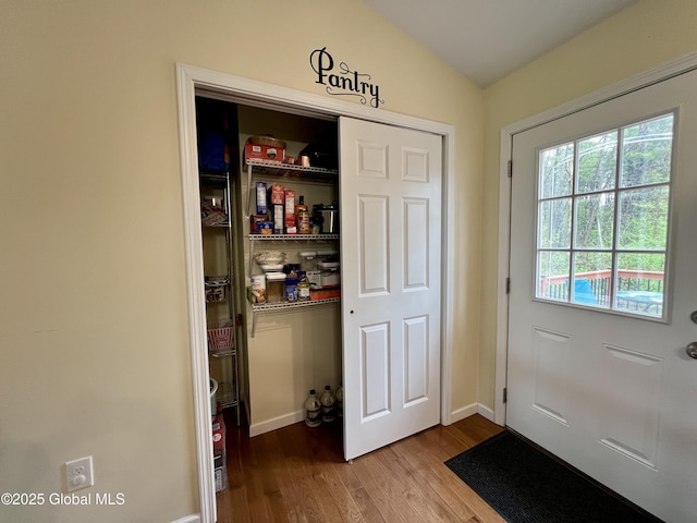 doorway with wood finished floors, lofted ceiling, and baseboards