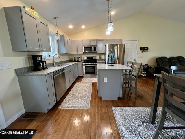 kitchen with stainless steel appliances, a sink, gray cabinets, lofted ceiling, and a kitchen breakfast bar