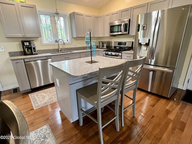 kitchen featuring appliances with stainless steel finishes, a sink, wood finished floors, a breakfast bar, and a center island with sink