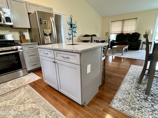 kitchen featuring stainless steel appliances, a breakfast bar area, gray cabinets, dark wood-style floors, and vaulted ceiling