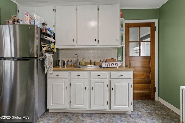 kitchen with freestanding refrigerator, a sink, decorative backsplash, white cabinetry, and crown molding