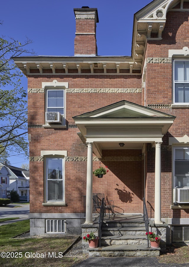 view of front of property with a chimney, cooling unit, and brick siding