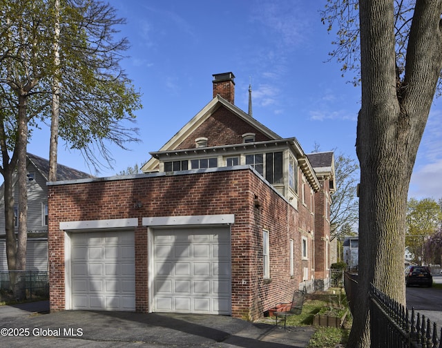 view of side of property featuring a chimney, driveway, brick siding, fence, and an attached garage