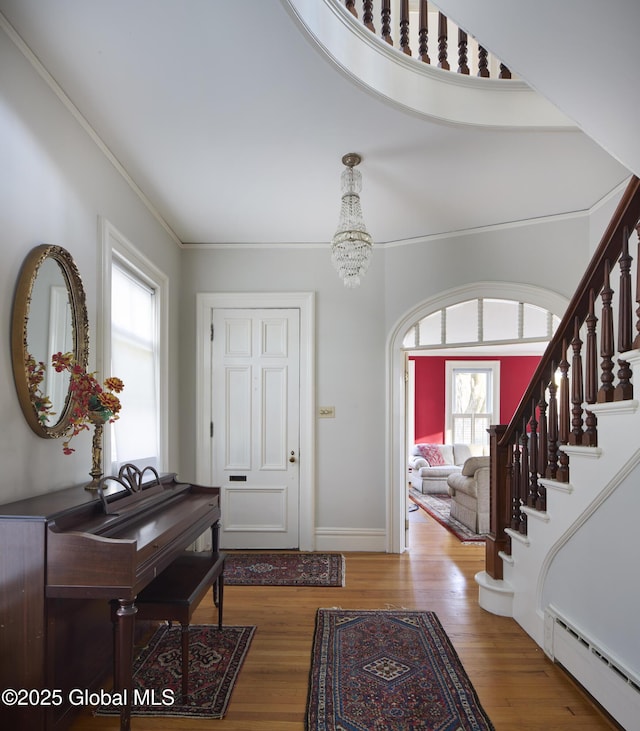 foyer featuring a notable chandelier, a baseboard heating unit, ornamental molding, stairs, and wood finished floors
