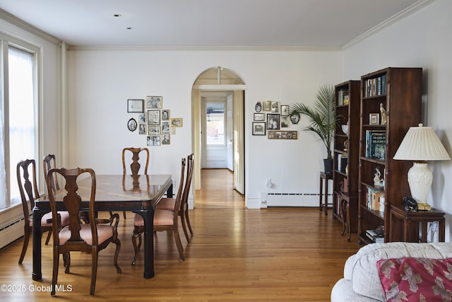 dining space featuring arched walkways, a baseboard radiator, ornamental molding, and wood finished floors