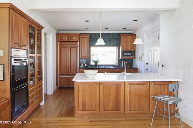 kitchen with a sink, ornamental molding, decorative light fixtures, black appliances, and light wood-style floors