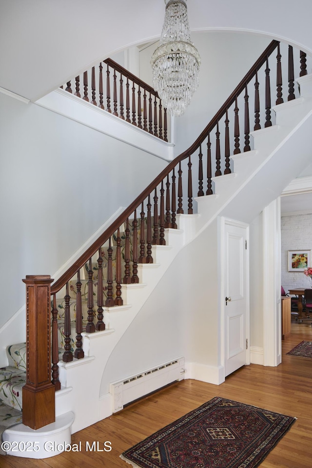 stairway featuring a chandelier, a towering ceiling, wood finished floors, and a baseboard heating unit