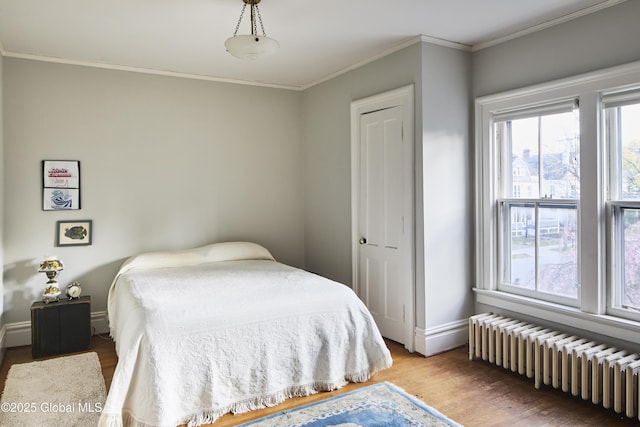 bedroom featuring crown molding, radiator, baseboards, and wood finished floors