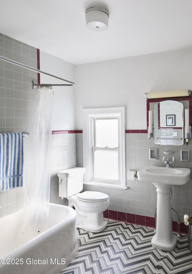 bathroom with tile walls, shower / tub combo, toilet, wainscoting, and tile patterned flooring