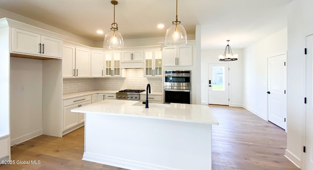 kitchen with double oven, a sink, backsplash, light wood-style flooring, and white cabinetry