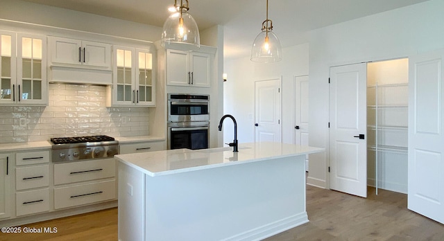 kitchen with appliances with stainless steel finishes, light wood-type flooring, decorative backsplash, pendant lighting, and white cabinetry