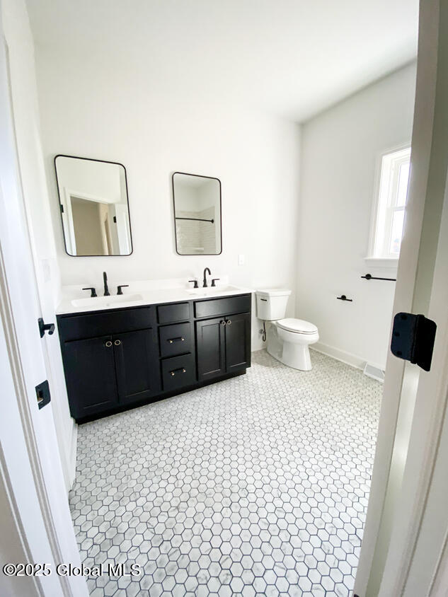 bathroom with toilet, double vanity, baseboards, and tile patterned floors