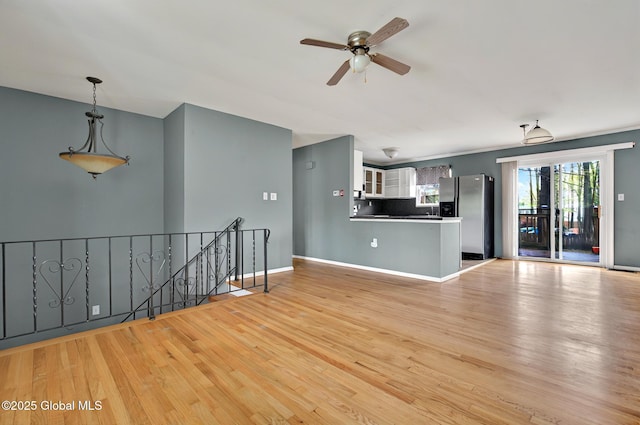 unfurnished living room with a ceiling fan, light wood-style flooring, and baseboards