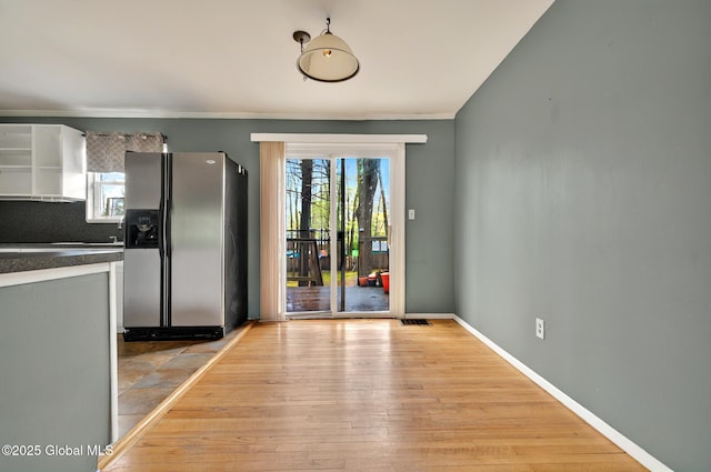 unfurnished dining area with light wood-style flooring, baseboards, and crown molding