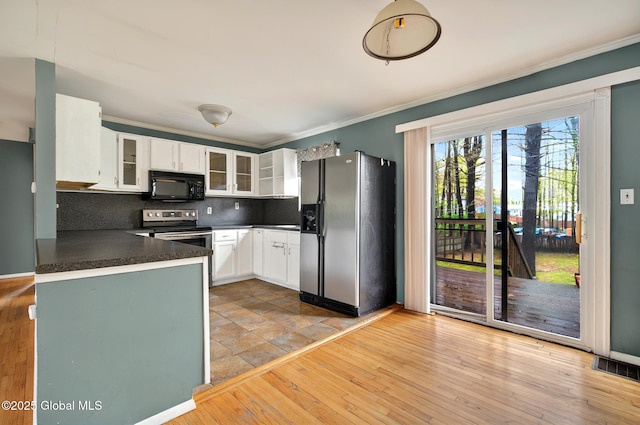 kitchen with appliances with stainless steel finishes, dark countertops, white cabinetry, glass insert cabinets, and decorative backsplash