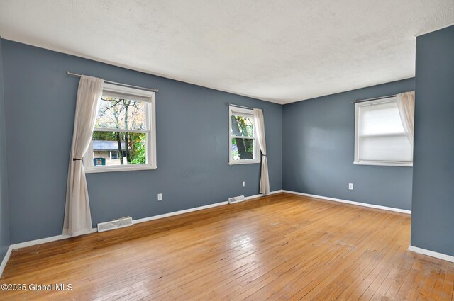 empty room with plenty of natural light, wood-type flooring, and baseboards