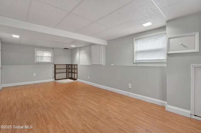 basement with a drop ceiling, baseboards, and light wood-style floors