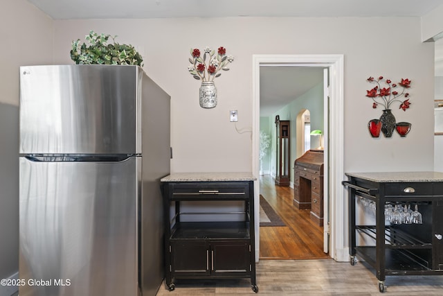 2125 Ferguson St, Rotterdam, NY 12303 - kitchen featuring freestanding refrigerator, light wood-type flooring, arched walkways, and light stone counters