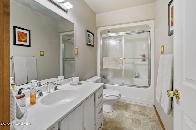bathroom featuring vanity, toilet, stone finish floors, and bath / shower combo with glass door