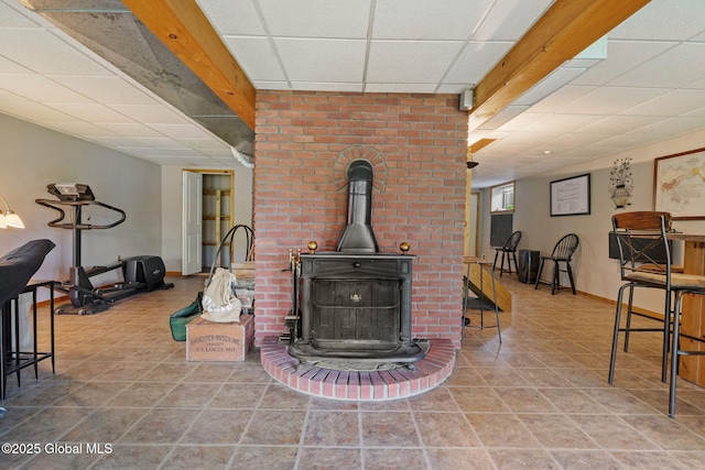 living area with a drop ceiling, baseboards, tile patterned floors, and a wood stove