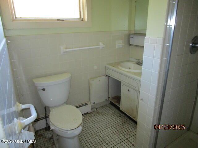 bathroom with a tile shower, tile walls, vanity, toilet, and a baseboard heating unit