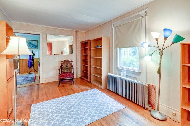 living area featuring radiator heating unit, hardwood / wood-style floors, baseboards, and crown molding