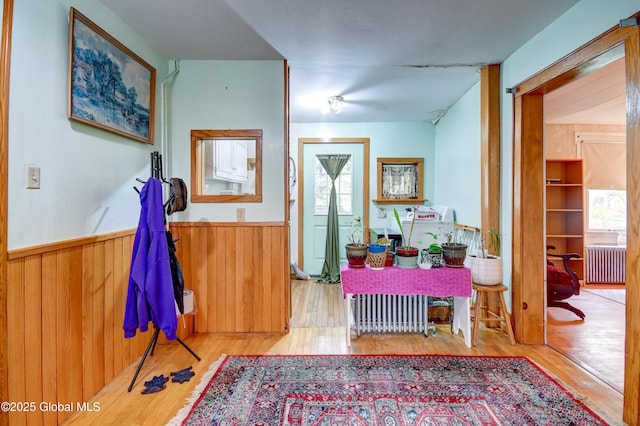hallway featuring radiator heating unit, a wainscoted wall, wood finished floors, and wood walls