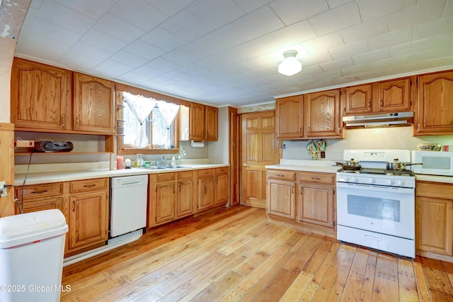 kitchen with white appliances, under cabinet range hood, light wood-style flooring, and light countertops