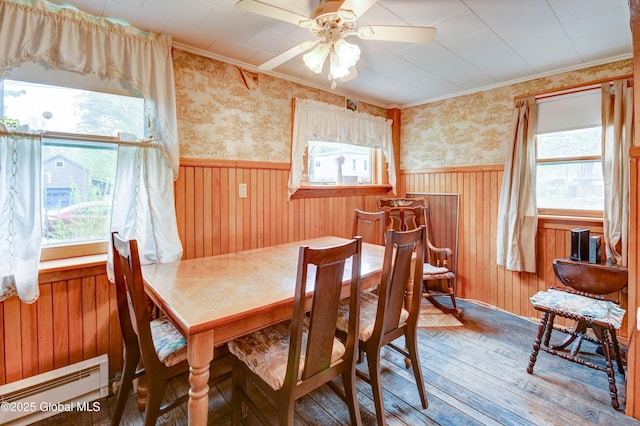 dining area with a baseboard radiator, wood-type flooring, wainscoting, ornamental molding, and wallpapered walls