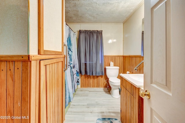 bathroom with wood finished floors, a textured ceiling, toilet, a wainscoted wall, and vanity