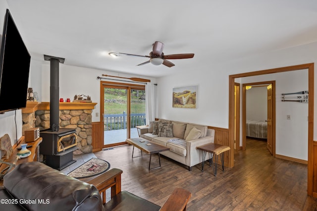 living room featuring wainscoting, wood finished floors, a ceiling fan, and a wood stove
