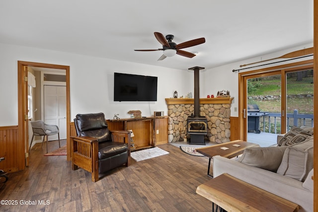 living room with wainscoting, a wood stove, wood finished floors, and a ceiling fan