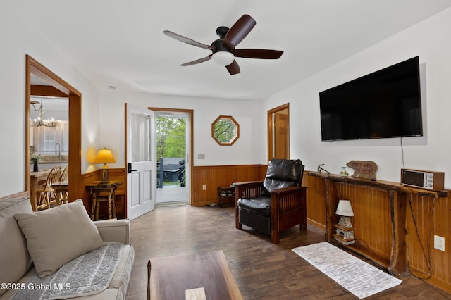 living area with wainscoting, dark wood-style flooring, a ceiling fan, a chandelier, and wooden walls