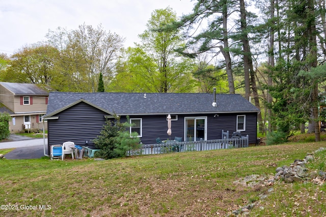 rear view of house with roof with shingles and a yard