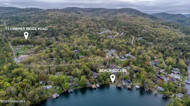 drone / aerial view of a heavily wooded area and a water and mountain view