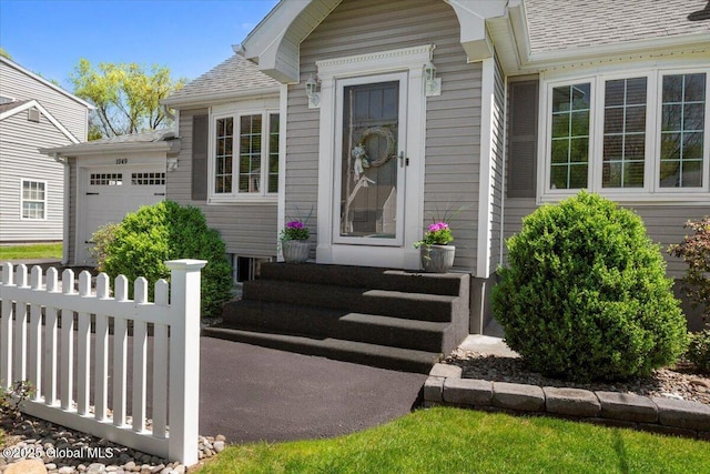 property entrance with a garage, fence, and roof with shingles