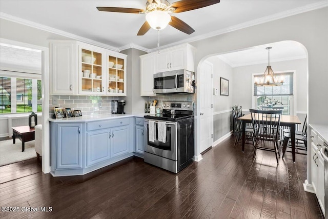 kitchen with appliances with stainless steel finishes, arched walkways, glass insert cabinets, a chandelier, and ornamental molding