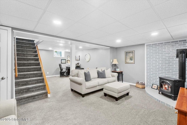 living area featuring a wood stove, carpet floors, a drop ceiling, stairs, and baseboards