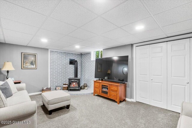 living area featuring a wood stove, carpet, baseboards, a drop ceiling, and recessed lighting