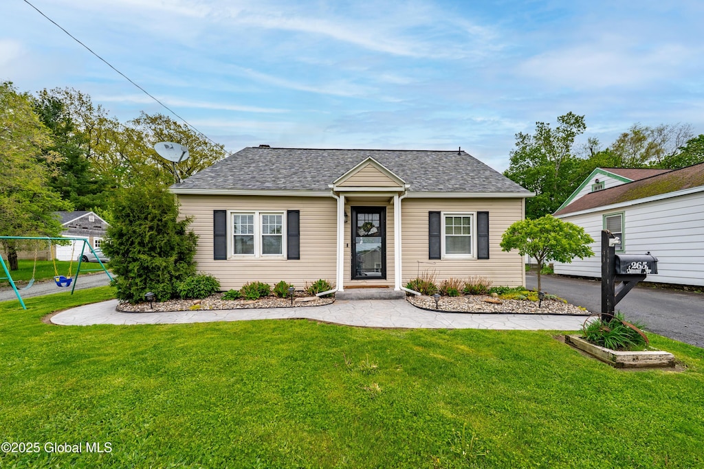 view of front of home with a front lawn, a shingled roof, and a playground