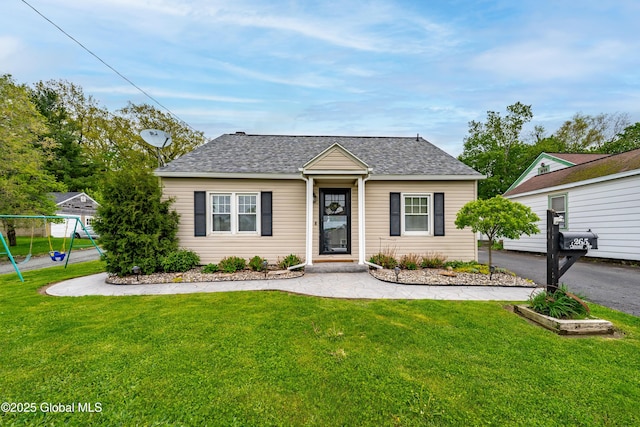 view of front of home with a front lawn, a shingled roof, and a playground