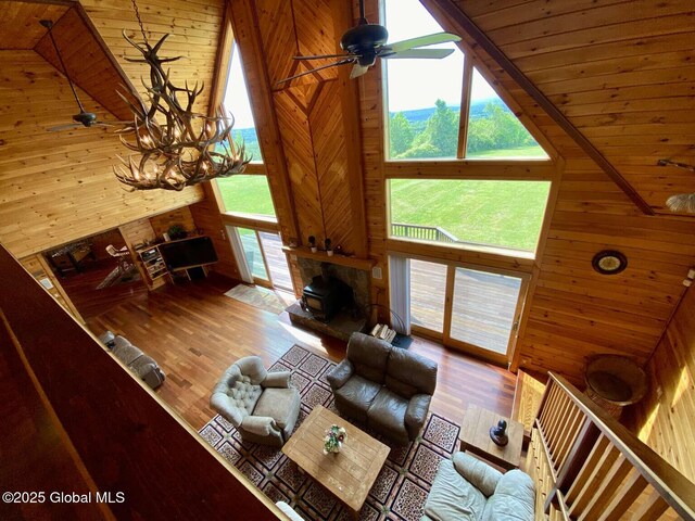 living room featuring high vaulted ceiling, wooden walls, ceiling fan, wood ceiling, and a wood stove