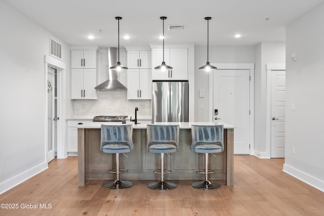 116 W Ave Unit 309, Saratoga Springs, NY 12866 - kitchen with freestanding refrigerator, wall chimney exhaust hood, a center island with sink, white cabinetry, and light countertops