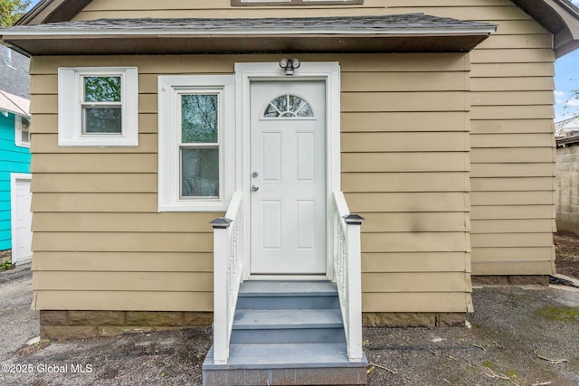 view of exterior entry with roof with shingles
