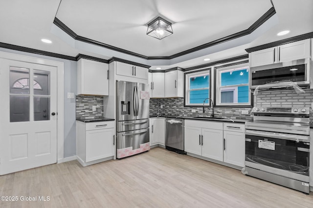 kitchen featuring appliances with stainless steel finishes, crown molding, a sink, dark countertops, and light wood-type flooring