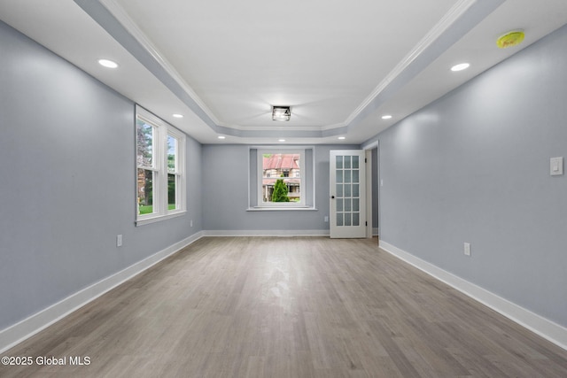 spare room with healthy amount of natural light, a raised ceiling, wood finished floors, ornamental molding, and baseboards