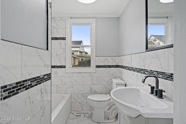 bathroom featuring tile walls, marble look tile flooring, toilet, a bath, and vanity