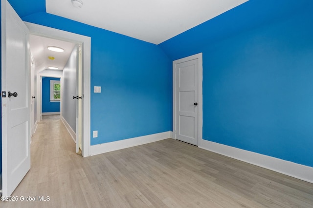 unfurnished room featuring light wood-style flooring, baseboards, a smoke detector, and vaulted ceiling