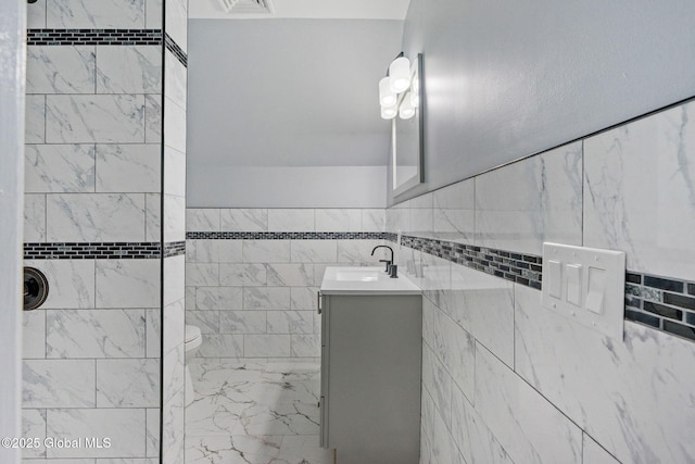 bathroom featuring vanity, a tile shower, tile walls, and toilet