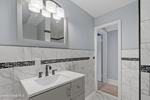 bathroom with marble look tile flooring, vanity, tile walls, and wainscoting